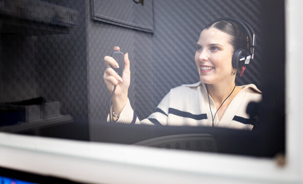 A grown girl is inside a soundproof audiometry booth. Young woman with positive expression wearing audiometric hearing aids while listening to tests.Young people lose their hearing.