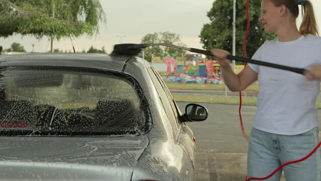 a girl with blond hair in a white T-shirt and jeans washes a car at a self-service car wash