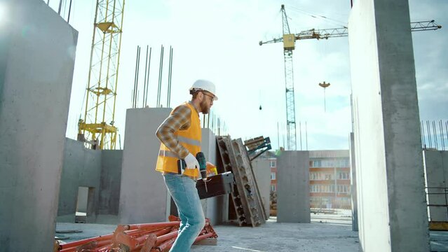 Happy construction worker at construction site dancing with boxtool and screwdriver. Enjoy the moment he wearing uniform and safety helmet. Looking at camera