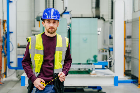portrait of a man in a helmet and overalls at a glass cutting and tempering plant against the background of a cutting machine.