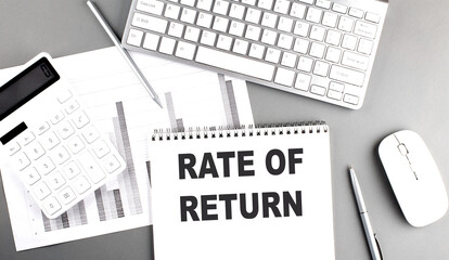 RATE OF RETURN text on a notebook with keyboard on grey background