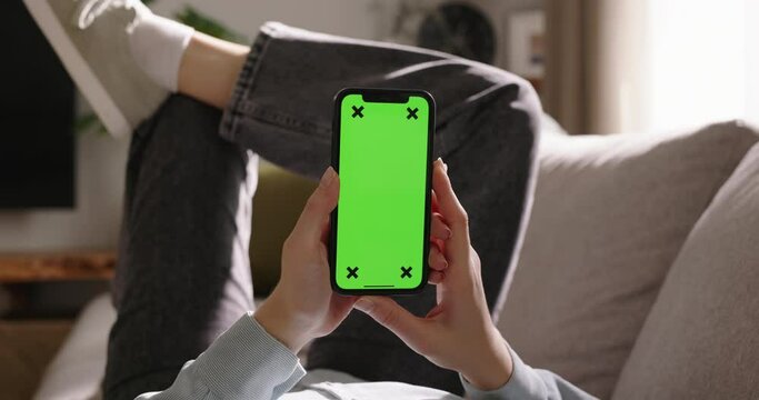 Young woman grips smartphone, displaying empty green screen, vertical mode. Advertising app. No touching. Engrossed in favorite movies video content, social media, digital realm. Endless possibilities