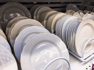 Plates for food in a stack, White color porcelain glass, stand in a stack on the shelf of a tableware store. concept selling tableware