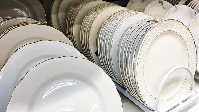 Plates for food in a stack, White color porcelain glass, stand in a stack on the shelf of a tableware store. concept selling tableware