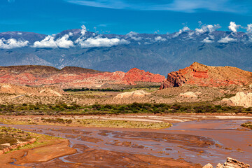 Landscape with a low-flow river with sandstone formations and mountains in the background.