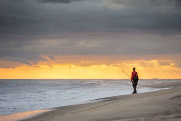 Fisherman on the beach surfcasting during a colorful sunset. Robert Moses State Park, Long Island,...