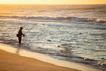 Fisherman silhouette on the beach surfcasting during a colorful sunrise. Robert Moses State Park,...