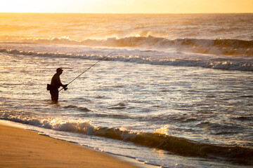 Fisherman silhouette on the beach surfcasting during a colorful sunrise. Robert Moses State Park,...