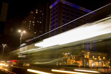 Fototapeta na wymiar Rastro das luzes de um ônibus coletivo circulando na Avenida Paulista a noite e a fundo prédio decorado com iluminação colorida. 
