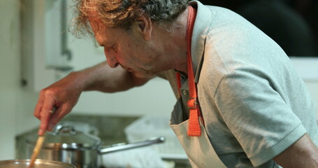 Older man preparing meal, senior person stirring pot while cooking at the kitchen