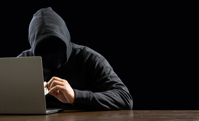 Hacker spy man one person black hoodie sitting on table hand holding credit card looking computer laptop used login password attack security data digital internet network system night dark background