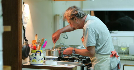 Senior man cooking at the kitchen. Candid older retired person stirring pot