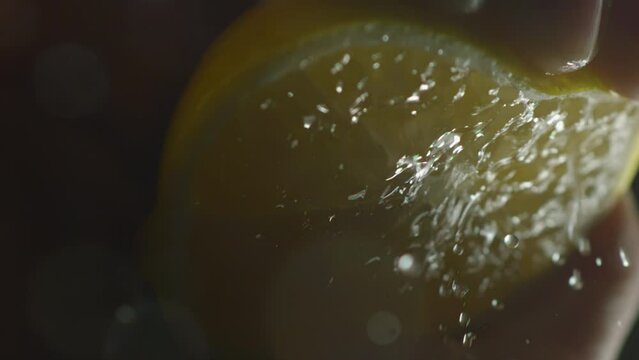 Hand of cook squeezing a lemon juice in slow motion. Macro of splash a citrus limonum juice against black background. Cooking food and drink concept