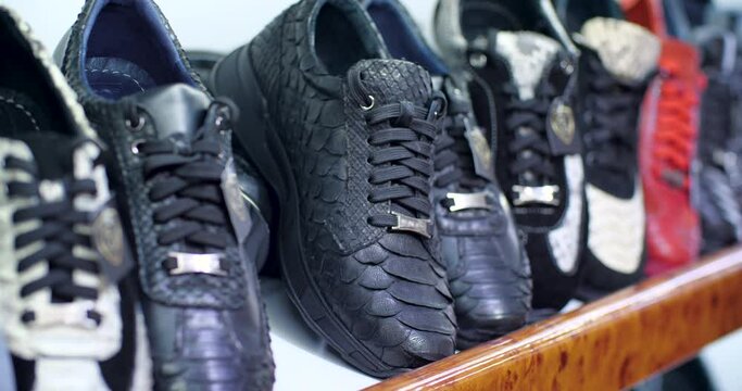 Man's hand takes a sneaker from shelf where they have sneakers with different natural leathers and puts it back on the shelf.