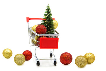 Artificial toy christmas tree and Christmas tree toys in supermarket grocery shopping cart isolated on white background. Winter holiday.