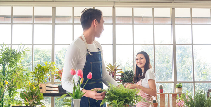 Portrait gardener young Asian man woman two person standing smiling enjoy looking hand holding help decorate tree leaf green in calm work shop home plant white wall. hobby job happy and care concept