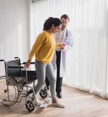 Fototapeta na wymiar Portrait latin american woman sick sit wheelchair with man doctor caucasian sitting two people check and treat patients talk helping support explain medicine sick person inside hospital room service