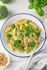 Vegetarian pasta with pesto sauce, broccoli, parmesan cheese and pine nuts on a white wooden background. Healthy food.