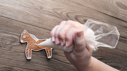 Cute gingerbread horse and human hand with piping bag on brown wooden background. Closeup of...