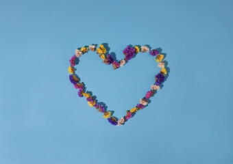 heart made of flowers on a blue background. flowers of different colors yellow pink white and purple
