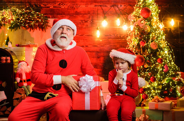 Thoughtful child boy and bearded man in Santa costume in room decorated for Christmas. New year...