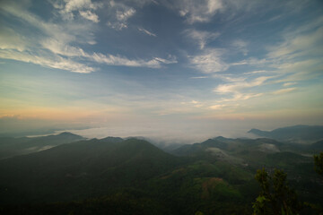 Obraz premium The stunning view from a tourist's standpoint as they go down a hill on a foggy trail with a hill and a background of a golden sky in Forest Park, Thailand. Bird's eye view. Aerial view. 