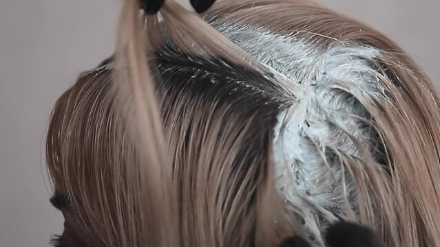 blonde paints over the dark hair roots on her head with hair dye, closeup
