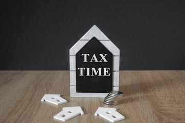 Black board in the shape of a house with words Tax Time near miniature house. Beautiful wooden table, copy space. Business and Tax Time concept.