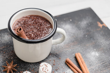Homemade spicy hot chocolate drink with cinnamon stick, grated chocolate in enamel cup on wooden table with white marshmallows and star anise