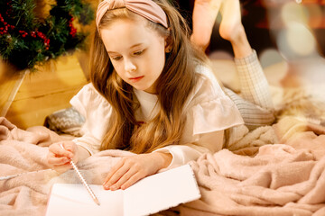 cute beautiful long-haired girl writing a letter to santa claus. New Year's atmosphere, make a...