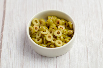 Chopped green olives in a white ceramic bowl, kitchen close-up.