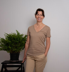 the simple and natural beauty of a radiant woman, dressed in beige tones, near a lush plant. Her...