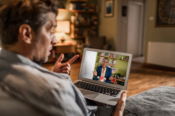 Young man talking to his financial advisor over a video call on his laptop in the living room of his home