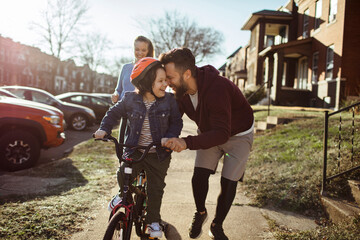 Happy little boy riding bike with parents outside
