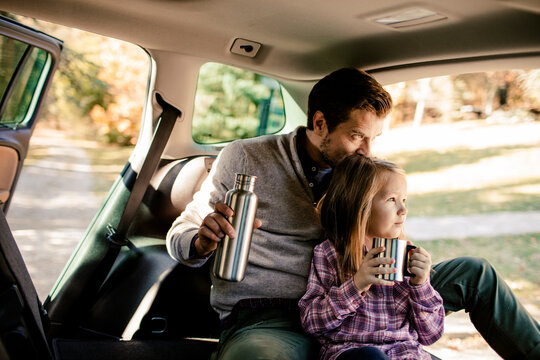Father and daughter having warm drink in car after camping