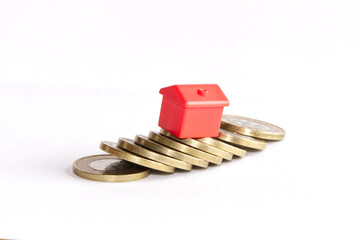 Single small red house standing on collapsed stack of coins on white background. 