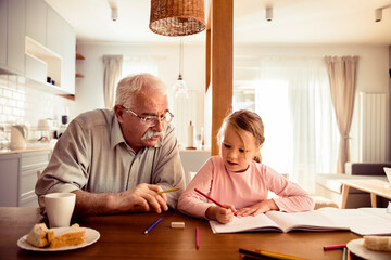 Grandfather helping little granddaughter with homework at home