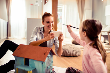 Little girl painting a doll house with her mother at home