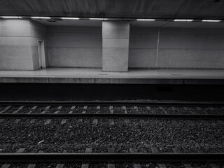 An empty black and white, well-lit subway station platform with clean, patterned walls and two sets...