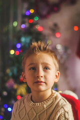 portrait of a cute boy in a sweater close-up in the room with a silhouette of a Christmas tree in the background