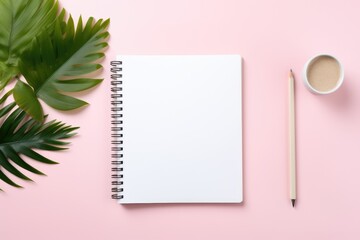 pleasing top view of a workspace with a blank notebook mockup, complemented by a wooden pencil, a cup of coffee, and vibrant green tropical leaves on a pink background