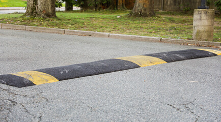 High-angle view of yellow speed bump on asphalt road, cautionary traffic sign nearby