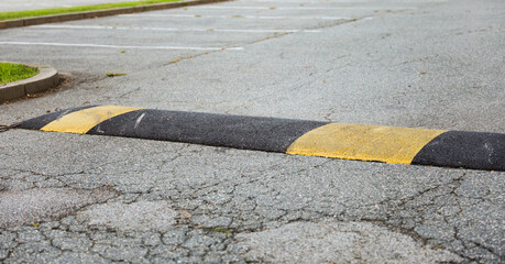 High-angle view of yellow speed bump on asphalt road, cautionary traffic sign nearby