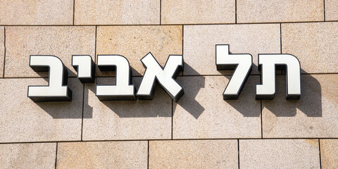Three-dimensional Hebrew letters on the tiled wall illuminated by the sun's rays and with shadows indicating the name of the city: Tel Aviv