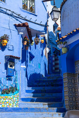 Narrow street with steps and some houses with old doors, all painted blue in the medina of Chefchaouen, Morocco