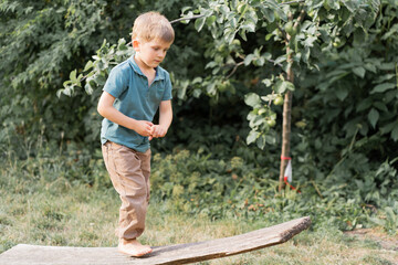 First steps to balance, nature's playground. Young boy on makeshift balance beam crafted from...