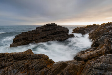 Wave flowing between two big rocks on the coastline.