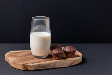 Wooden board with a glass of milk and muffins on a black background, chocolate muffins and a glass of milk