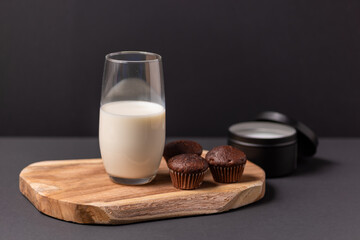 Wooden board with a glass of milk and muffins on a black background, chocolate muffins and a glass of milk