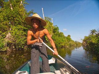 asian man in straw hat paddles down river in canoe
